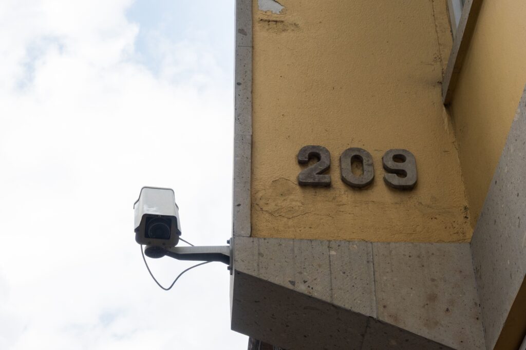 Close-up view of a yellow building corner with a security camera and address number 209 in Toluca, Mexico.
